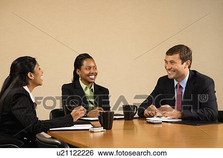 Businesspeople sitting at conference table talking and smiling View Large Photo Image Stock Photograph - Businesspeople sitting at conference table talking and smiling. Fotosearch
