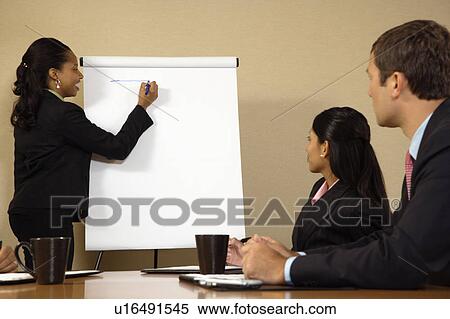 Stock Photography - Businesspeople sitting at conference table while businesswoman gives presentation. Fotosearch