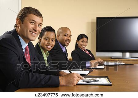 Stock Photography - Businesspeople sitting at conference table smiling with flat screen . Fotosearch