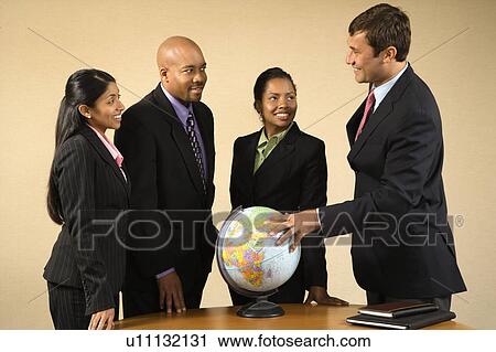 Stock Image - Corporate businesspeople standing around world globe smiling and talking.. Fotosearch