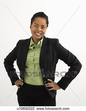 Stock Image - Portrait of smiling businesswoman with hands on hips against white background.. Fotosearch