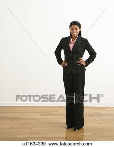 Stock Image - Portrait of smiling businesswoman with hands on hips against white background.. Fotosearch