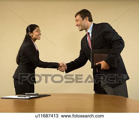 Stock Image - Two businesspeople in suits shaking hands and smiling. Fotosearch