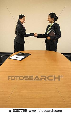 Stock Photograph - Two businesswomen in suits shaking hands and smiling. Fotosearch