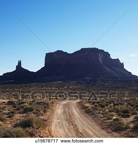 Stock Photo - Dirt road headed toward rock formations in desert of Monument Valley, Utah.. Fotosearch