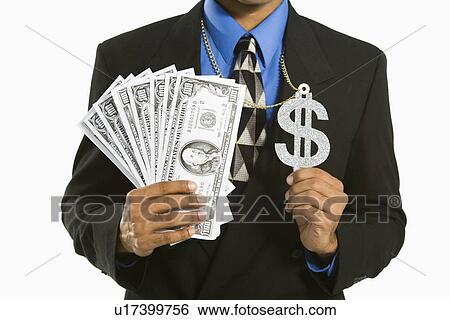 Stock Photograph - African American man in suit wearing necklace with money sign and holding cash.. Fotosearch