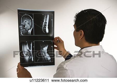 Stock Image - Asian American male doctor examining x-rays.. Fotosearch