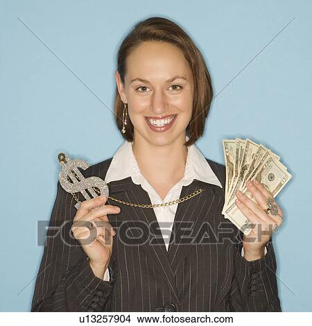 Picture - Caucasian businesswoman smiling holding money and wearing necklace with oversized dollar sign.. Fotosearch
