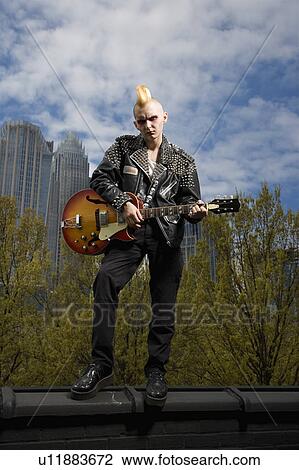 Stock Image - Male punk holding guitar with skyline . Fotosearch