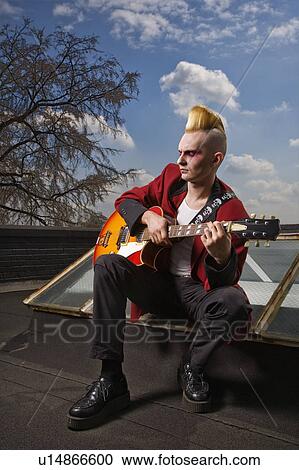 Stock Image - Male punk sitting on a skylight playing guitar. Fotosearch