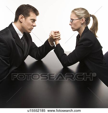 Stock Photography - Side view of Caucasian mid-adult businessman and businesswoman arm wrestling on table.. Fotosearch