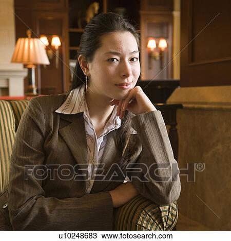 Stock Image - Taiwanese mid adult buisinesswoman looking at viewer with head resting on hand.. Fotosearch