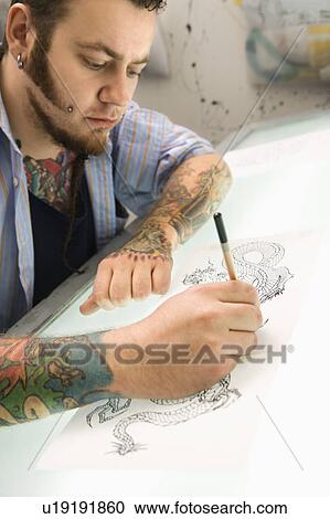 Stock Image - Tattoo artist drawing tattoo on light table. Fotosearch