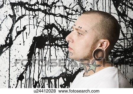 Stock Photo - Tattooed and pierced man against paint splattered background.. Fotosearch