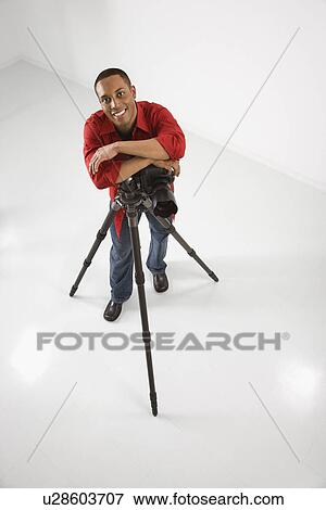 Stock Photo - Young African American male adult photographer posing with camera and tripod.. Fotosearch