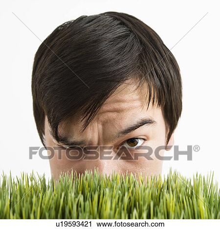 Stock Image - Asian young man looking over grass with eyebrow cocked.. Fotosearch