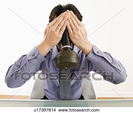 Picture - Businessman sitting wearing gas mask holding his hands over his eyes.. Fotosearch