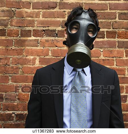 Stock Image - Businessman standing next to brick wall wearing gas mask. Fotosearch