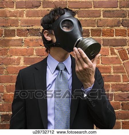 Stock Image - Businessman standing next to brick wall wearing gas mask. Fotosearch