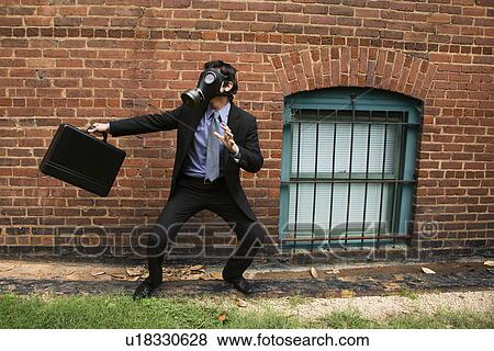 Stock Photo - Businessman standing next to brick wall wearing gas mask in fighting stance. Fotosearch