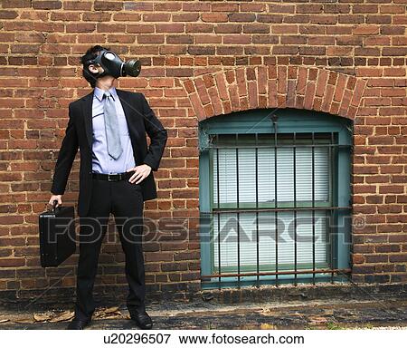 Stock Photo - Businessman standing next to brick wall and looking off to side wearing gas mask.. Fotosearch
