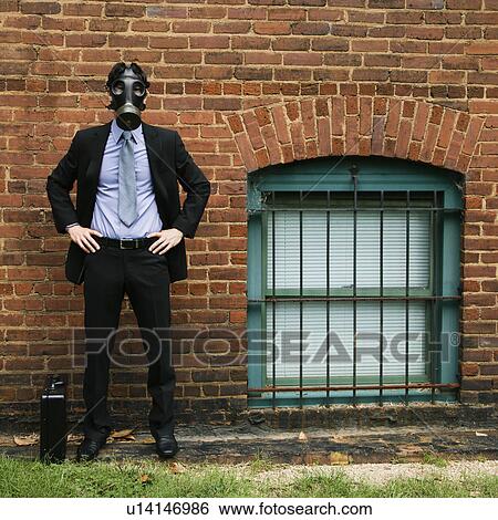 Stock Photograph - Businessman standing next to brick wall wearing gas mask. Fotosearch