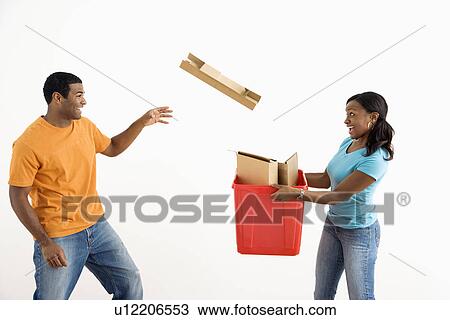 Stock Image - Female holding recycling bin while male tosses cardboard into it. Fotosearch