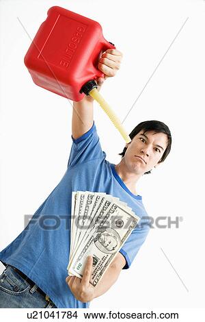 Picture - Man holding gas can pouring gasoline onto money. Fotosearch