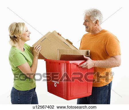 Stock Image - Man holding recycling bin while woman places cardboard into it. Fotosearch