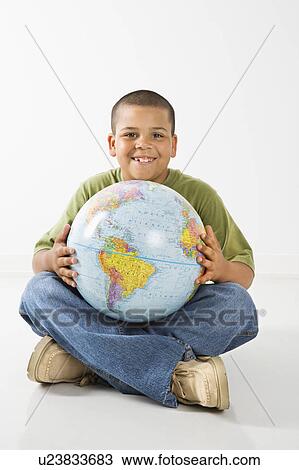 Stock Image - Young latino adolescent boy sitting with globe.. Fotosearch