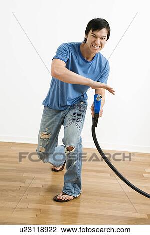 Stock Image - Young man aiming gasoline pump nozzle like a gun. Fotosearch