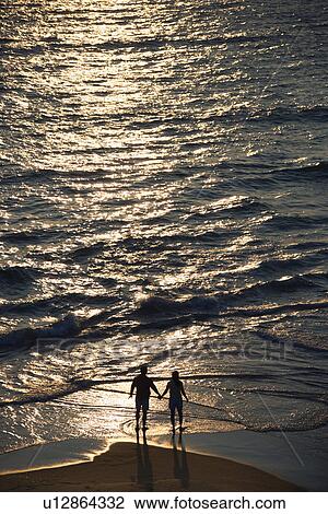 Stock Image - Aerial view of couple holding hands on beach in Bald Head Island, North Carolina at sunset. Fotosearch