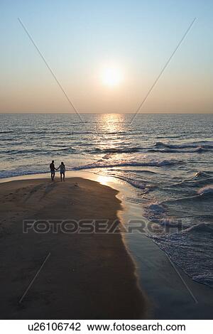 Stock Image - Aerial view of couple holding hands on beach in Bald Head Island, North Carolina at sunset.. Fotosearch