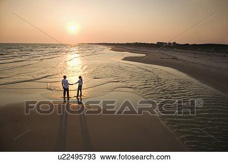 Stock Image - Aerial view of romantic couple standing on beach holding hands on Bald Head Island, North Carolina.. Fotosearch