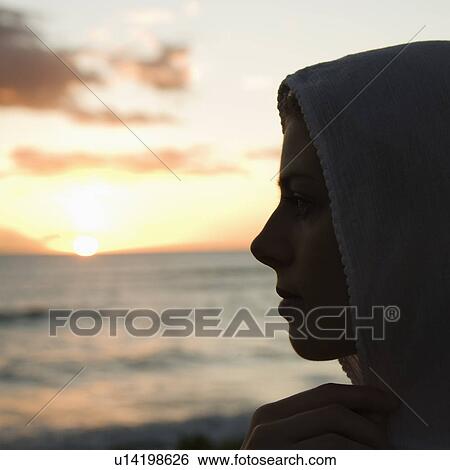 Stock Photograph - Woman with scarf over head profiled against sunset over ocean. Fotosearch