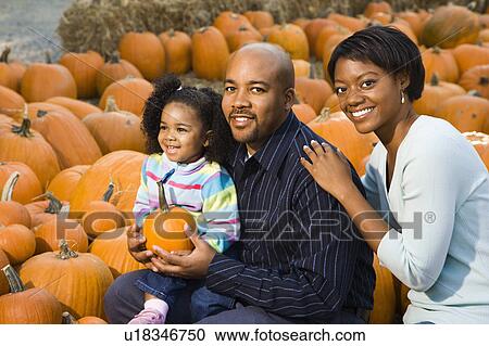 Stock Image - Parents and daughter picking out pumpkin and smiling at outdoor market.. Fotosearch