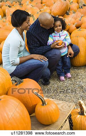 Stock Photo - Parents and daughter picking out pumpkin and smiling at outdoor market.. Fotosearch