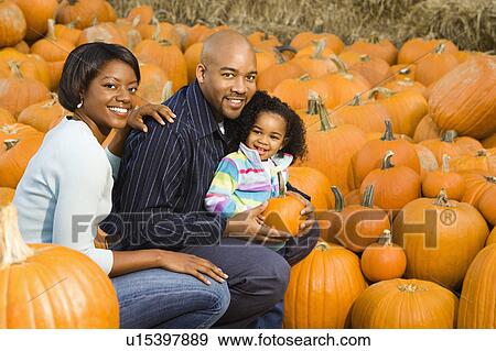 Stock Photo - Parents and daughter picking out pumpkin and smiling at outdoor market. Fotosearch