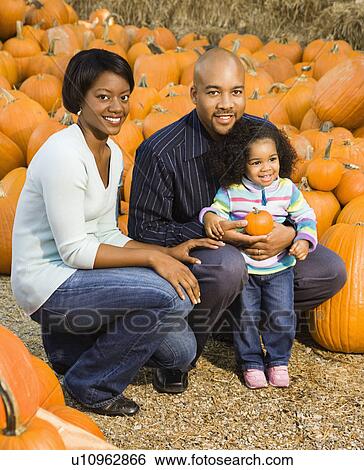 Stock Photograph - Parents and daughter picking out pumpkin at outdoor market. Fotosearch