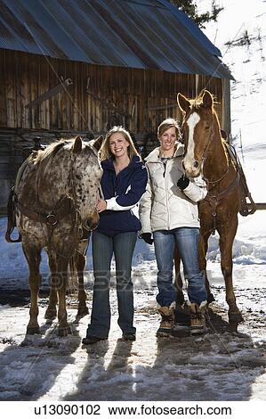 Two Caucasian women holding horses smiling at viewer with stable in background. View Large Photo Image Stock Image - Two Caucasian women holding horses smiling at viewer with stable in background.. Fotosearch