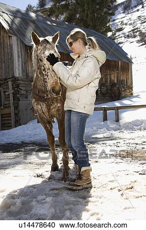 Stock Image - Woman petting horse with stable. Fotosearch