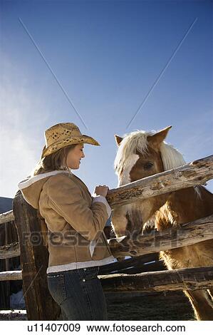 Stock Photo - Woman standing at fence with horse. Fotosearch