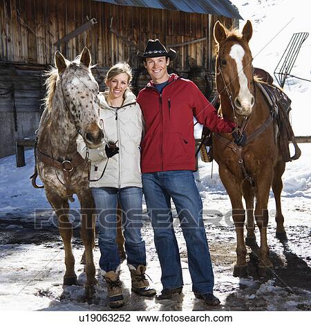 Caucasian couple holding horses in winter with stable in background. View Large Photo Image Stock Image - Caucasian couple holding horses in winter with stable in background.. Fotosearch