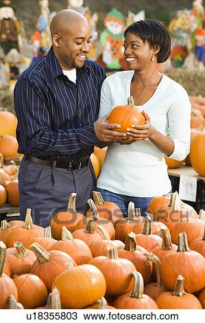 Stock Image - Couple picking out pumpkins and smiling at outdoor market. Fotosearch