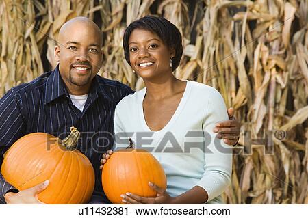 Happy smiling couple sitting on hay bales and holding pumpkins View Large Photo Image Stock Image - Happy smiling couple sitting on hay bales and holding pumpkins. Fotosearch