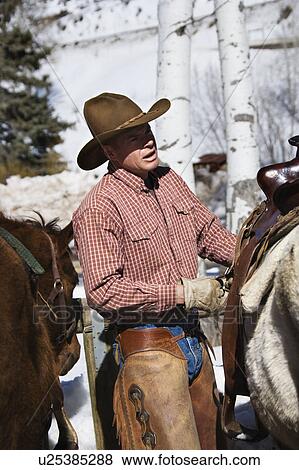 Male wrangler putting saddle on horse View Large Photo Image Stock Photo - Male wrangler putting saddle on horse. Fotosearch