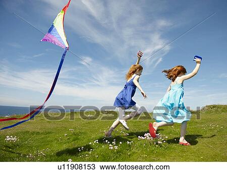 Stock Image - 2 young girls running with kites. Fotosearch
