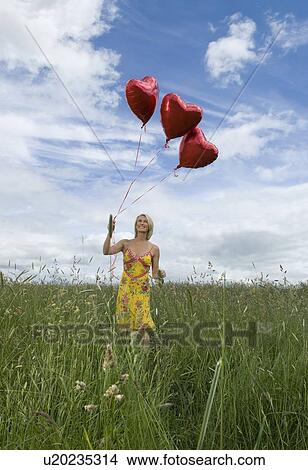 Picture - Smiling woman in field with balloons. Fotosearch