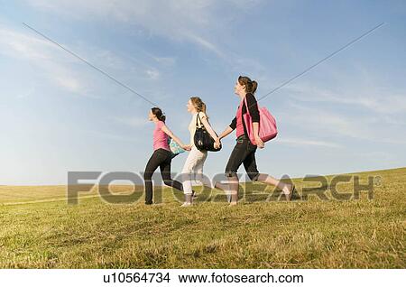Three girls walking over a grass hill View Large Photo Image Picture - Three girls walking over a grass hill. Fotosearch