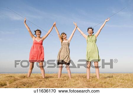 Stock Image - Three teenage girls hold hands up high. Fotosearch